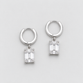 A pair of silver huggie hoop earrings with rectangular emerald-cut clear gemstones, displayed on a clean light gray background.