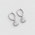 A pair of silver huggie hoop earrings with small pavé-set round stones along the front and a larger round center stone dangling below each hoop, shown on a light gray background.