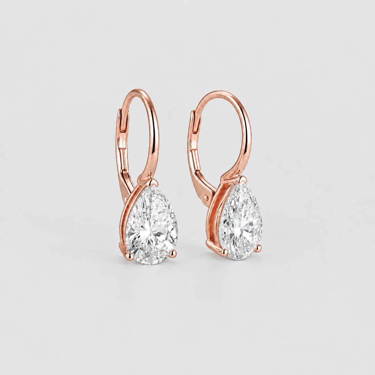 A pair of rose gold leverback hoop earrings with pear-cut clear gemstones, displayed on a clean light gray background.