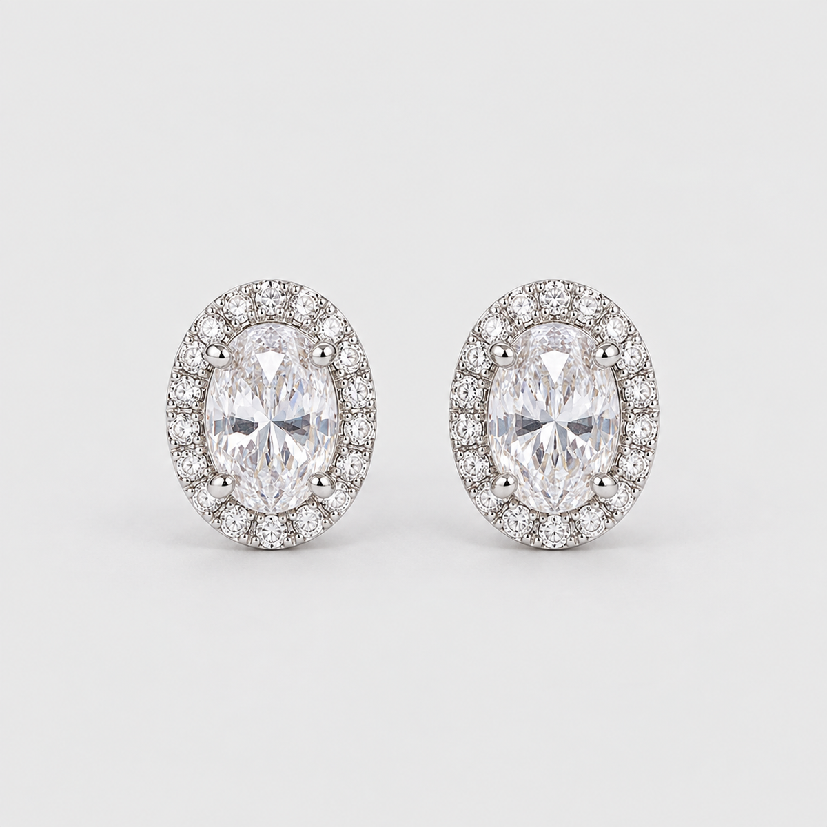 A pair of oval halo stud earrings featuring marquise-cut center stones surrounded by small round stones in a silver-toned setting, photographed on a light gray background.