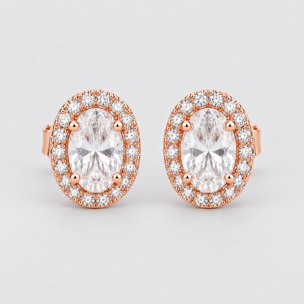A pair of rose gold halo stud earrings featuring oval-cut clear center stones surrounded by a halo of small round clear stones, set against a light gray background.