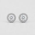 A pair of round diamond halo stud earrings in silver-toned metal, featuring a central round diamond surrounded by a halo of smaller diamonds, set against a clean light gray background.