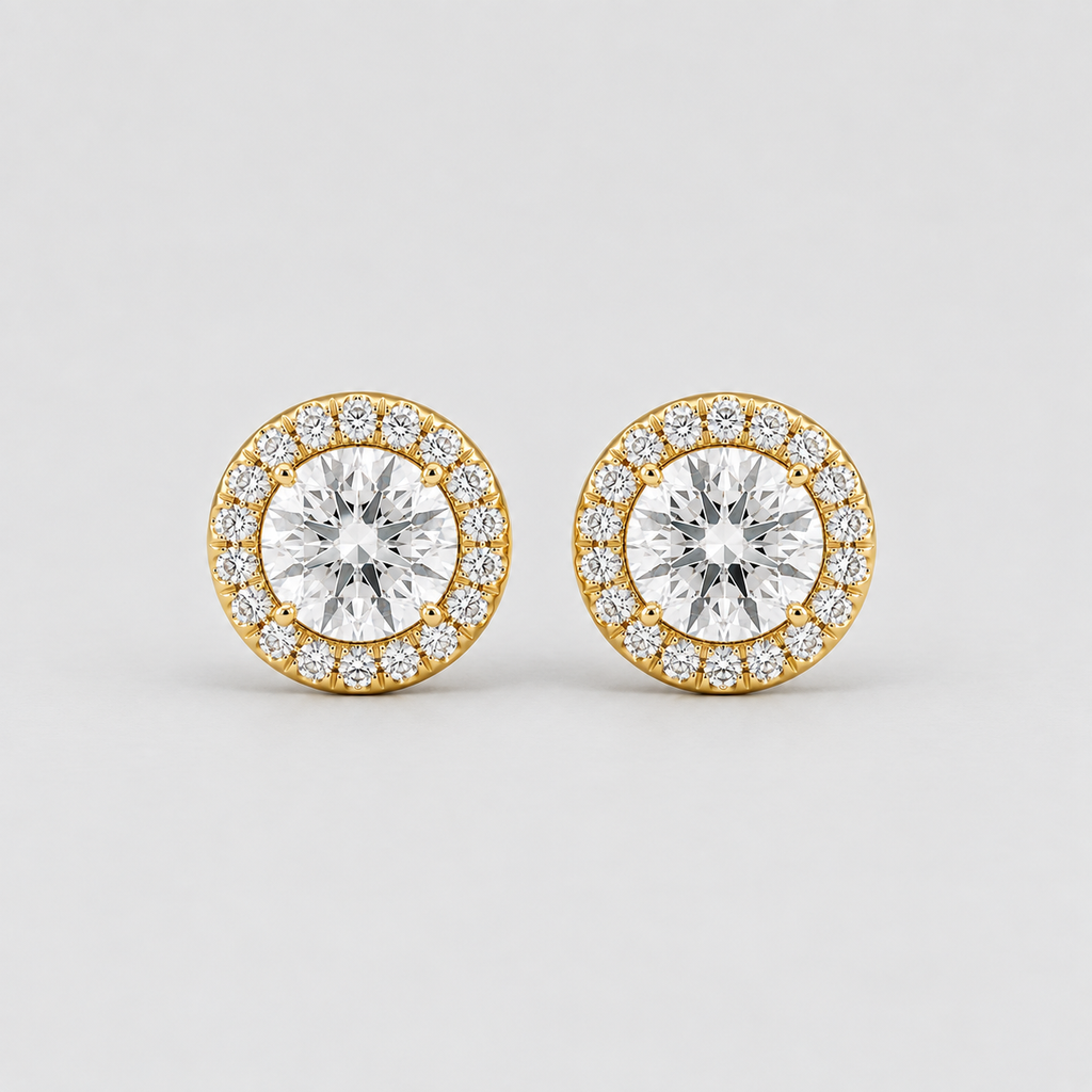 A pair of round yellow gold stud earrings, each featuring a large central clear round-cut gemstone surrounded by a halo of smaller clear pavé-set gemstones, photographed on a light gray background.