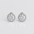 A pair of round halo stud earrings with large clear center stones and a border of smaller clear stones in a silver-toned setting, photographed on a clean light gray background.
