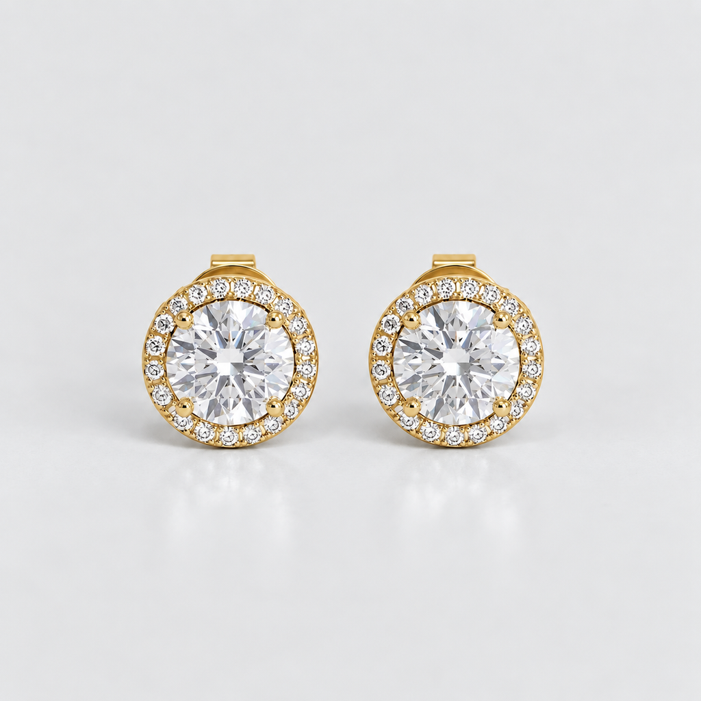 A pair of gold round stud earrings with a halo of small clear stones surrounding a larger central clear gemstone, shown on a light gray reflective background.