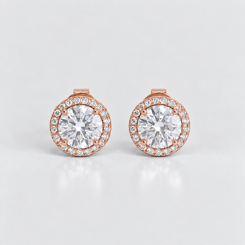 A pair of rose gold stud earrings with a halo setting, featuring a large round clear center stone surrounded by a border of smaller round stones, set against a light gray background.