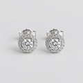 A pair of round halo stud earrings with large clear center stones and a surrounding halo of smaller clear stones in a silver-toned setting, photographed on a light gray background.