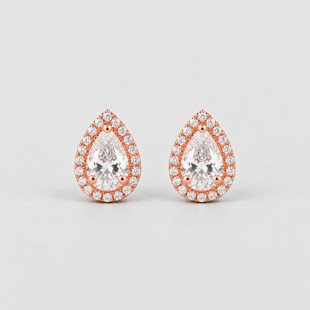 A pair of pear-shaped stud earrings in rose gold with a halo of small clear stones around a larger central clear stone, shown on a light gray background.