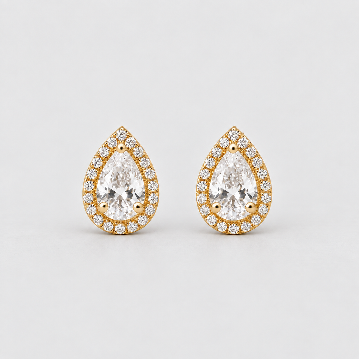 A pair of gold teardrop-shaped stud earrings with clear gemstones, photographed on a clean light gray background.