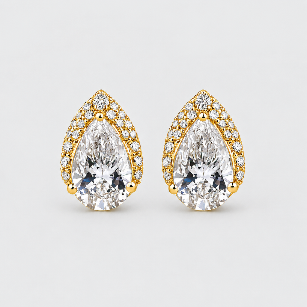 A pair of pear-shaped gold stud earrings with large clear center stones and smaller clear stones along the border, shown on a light gray background.