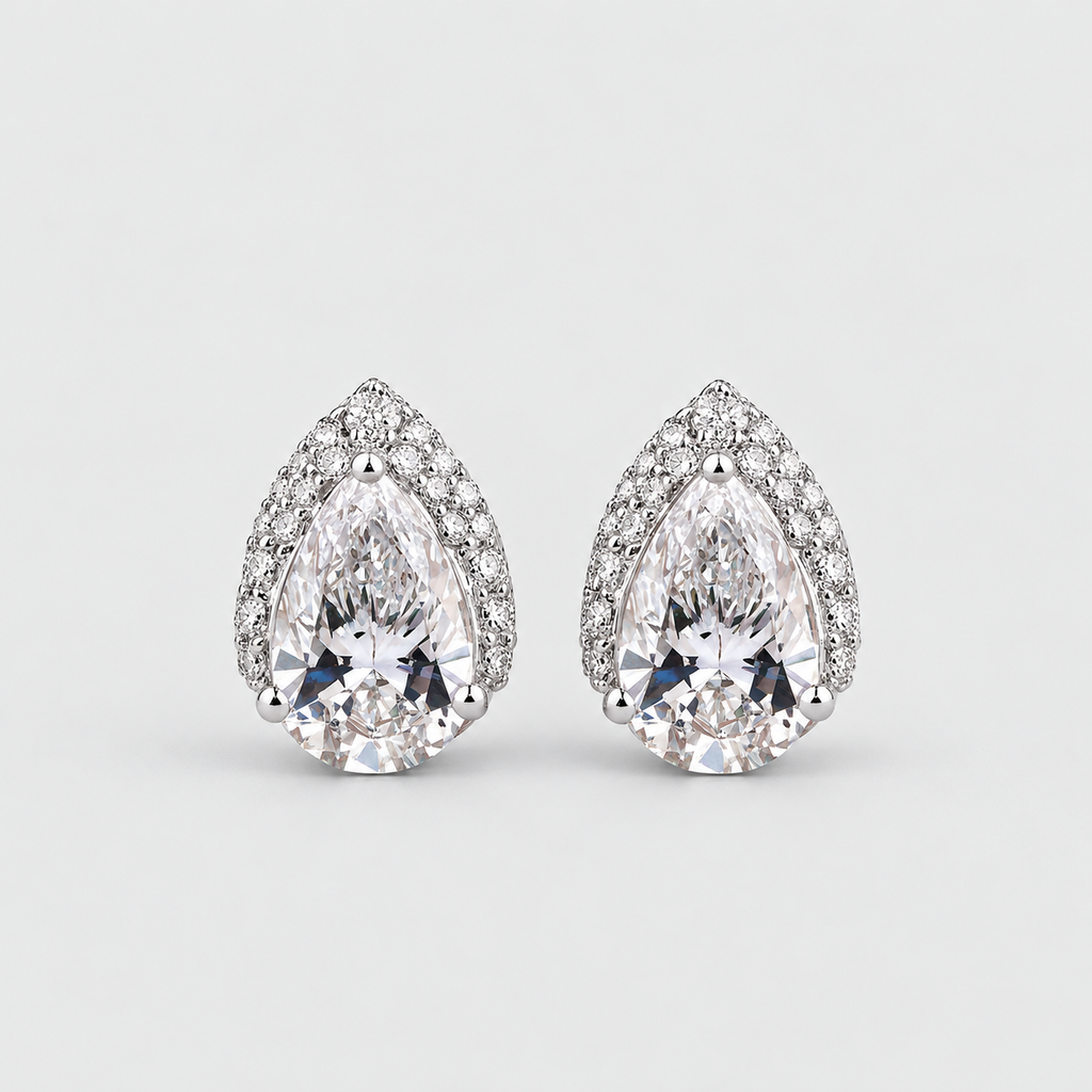 A pair of pear-shaped diamond stud earrings in a silver-toned setting, surrounded by small round diamonds, on a light gray background.