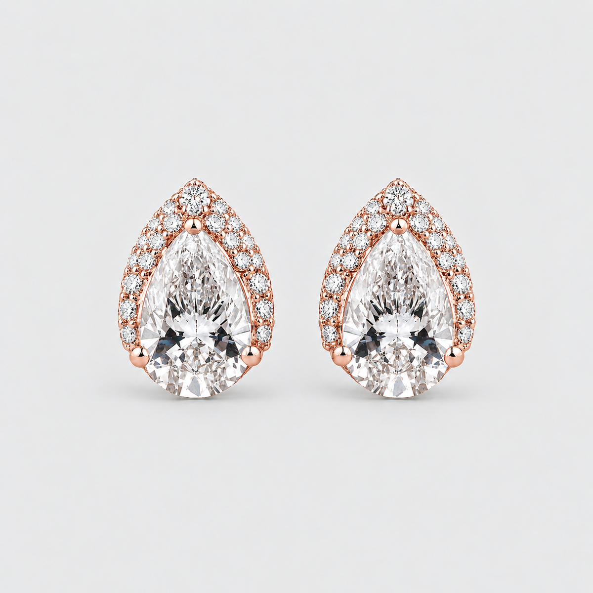 A pair of pear-shaped rose gold stud earrings with clear gemstones, set against a light gray background.