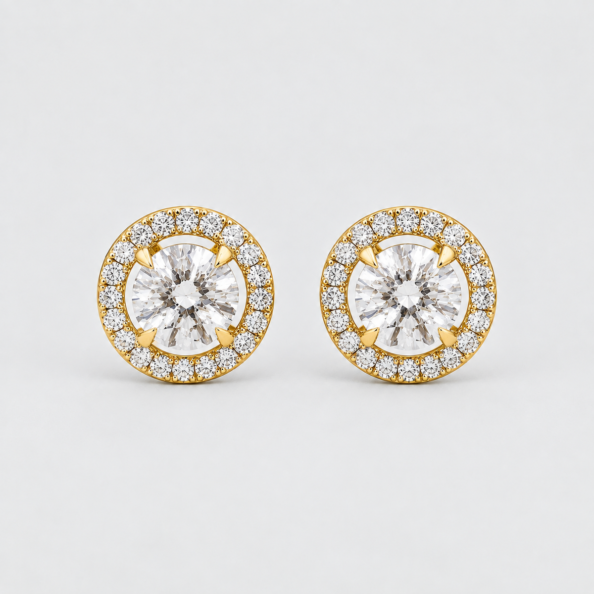A pair of round yellow gold halo stud earrings with clear gemstones, photographed on a clean light gray background.
