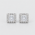 A pair of square stud earrings featuring a princess-cut clear center stone surrounded by a halo of smaller clear stones, set in a silver-toned metal on a light gray background.