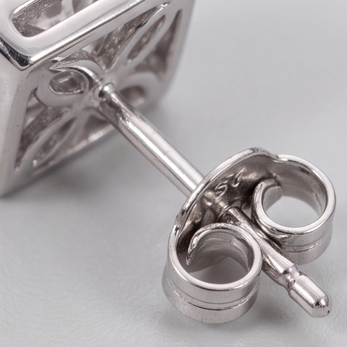 Close-up of a silver stud earring showing the back setting and butterfly clutch, on a light gray background.