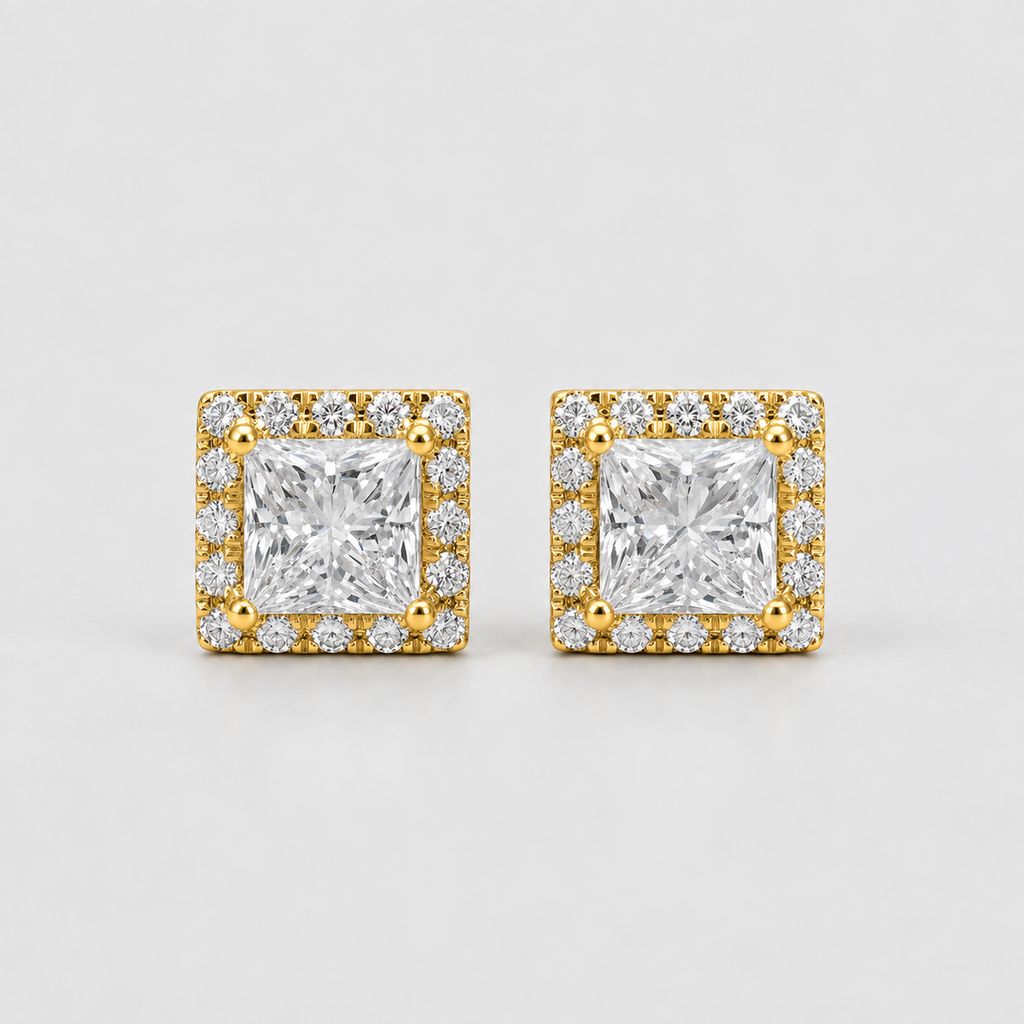 A pair of square stud earrings featuring a central princess-cut clear gemstone surrounded by a halo of smaller clear stones in a yellow gold setting, photographed on a light gray background.