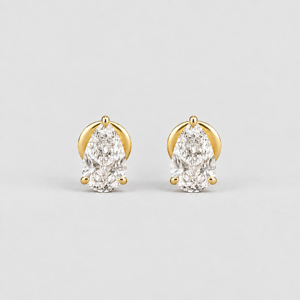 A pair of gold stud earrings with pear-cut clear gemstones, photographed on a clean light gray background.