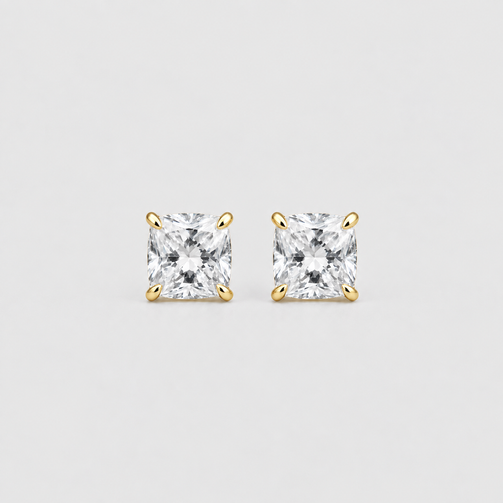A pair of gold stud earrings with princess-cut clear gemstones, set against a solid light gray background.