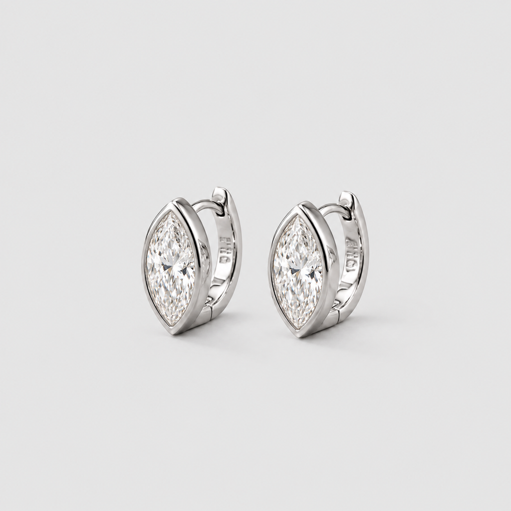 A pair of silver-toned huggie hoop earrings with marquise-cut clear gemstones, displayed on a light gray background.