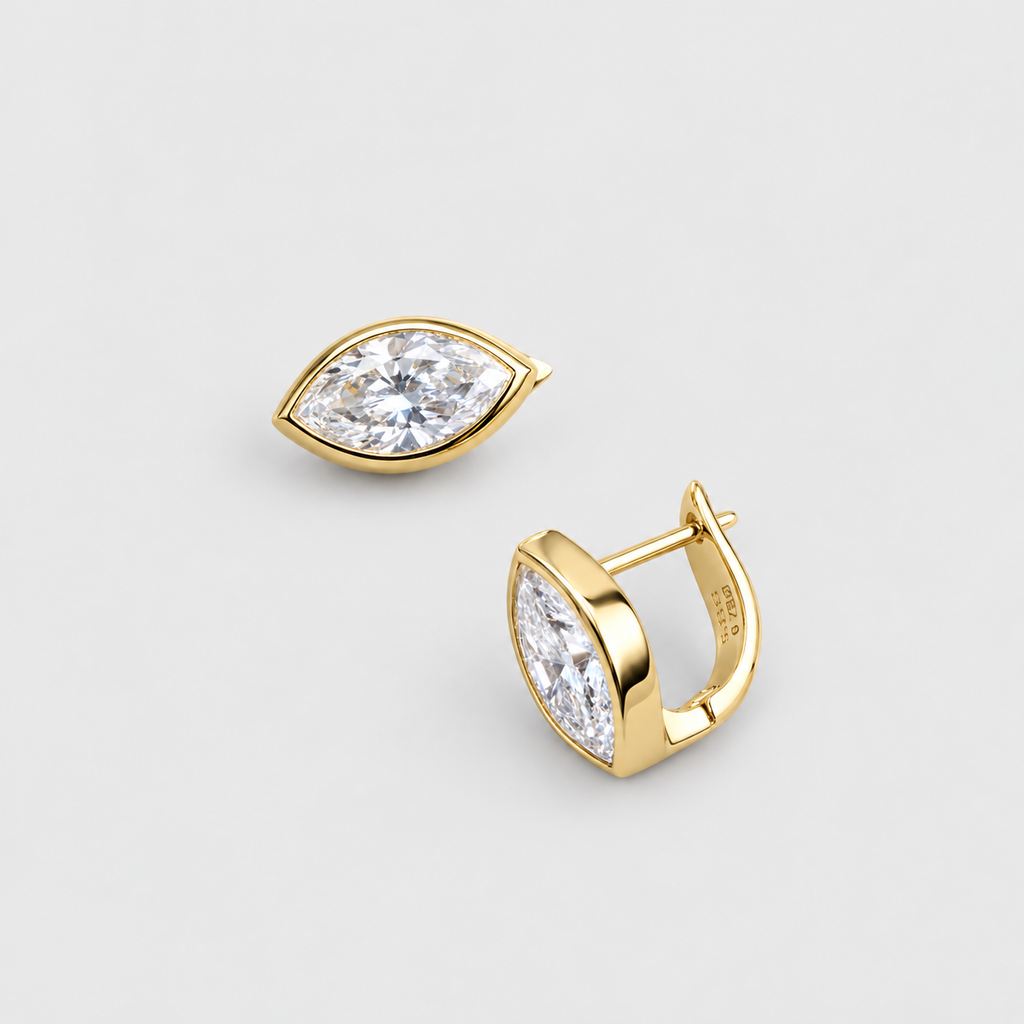 A pair of gold huggie hoop earrings with marquise-cut clear gemstones, shown on a light gray background. One earring is facing forward, and the other is angled to show the side profile and post.