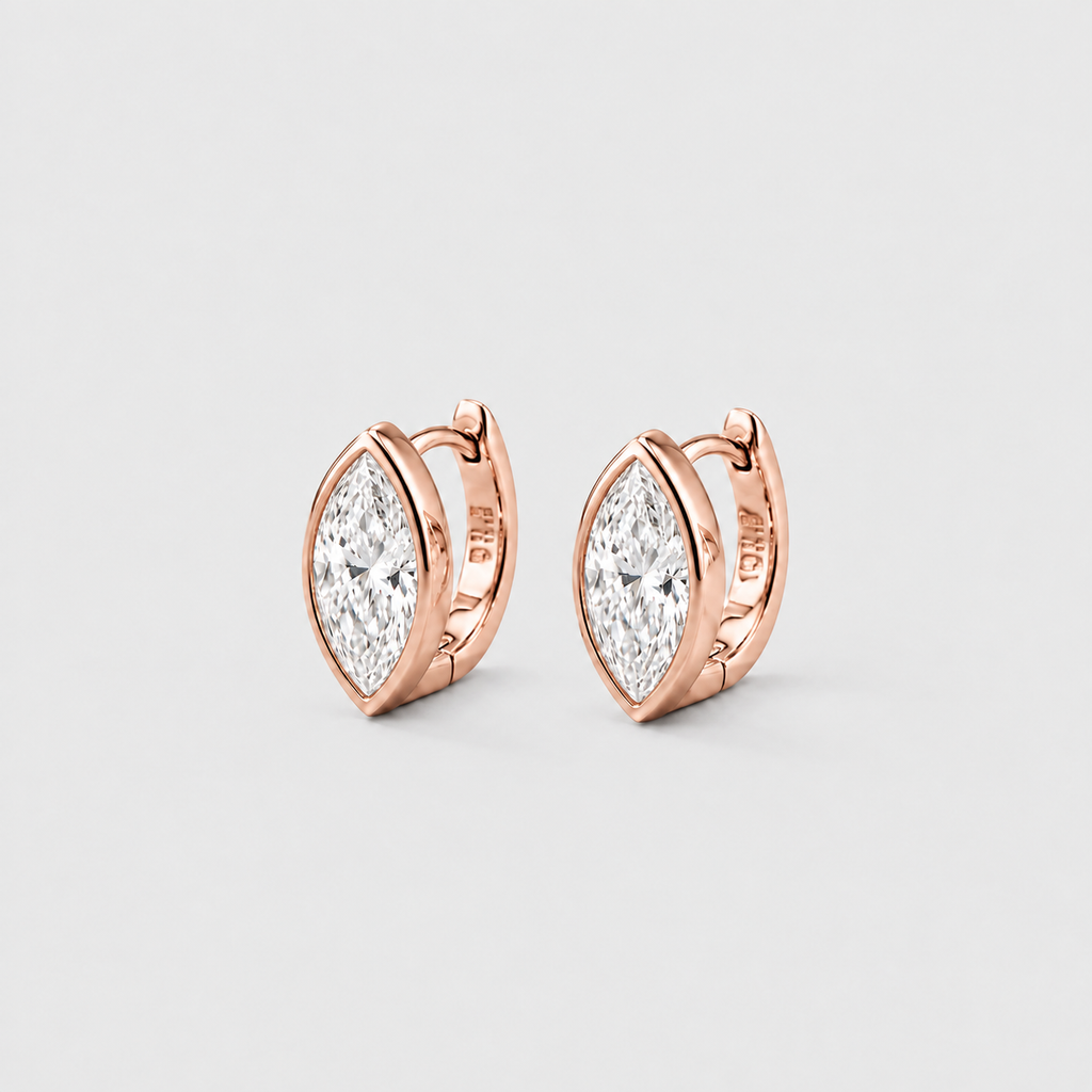 A pair of rose gold huggie hoop earrings with marquise-cut clear gemstones, shown on a light gray background.