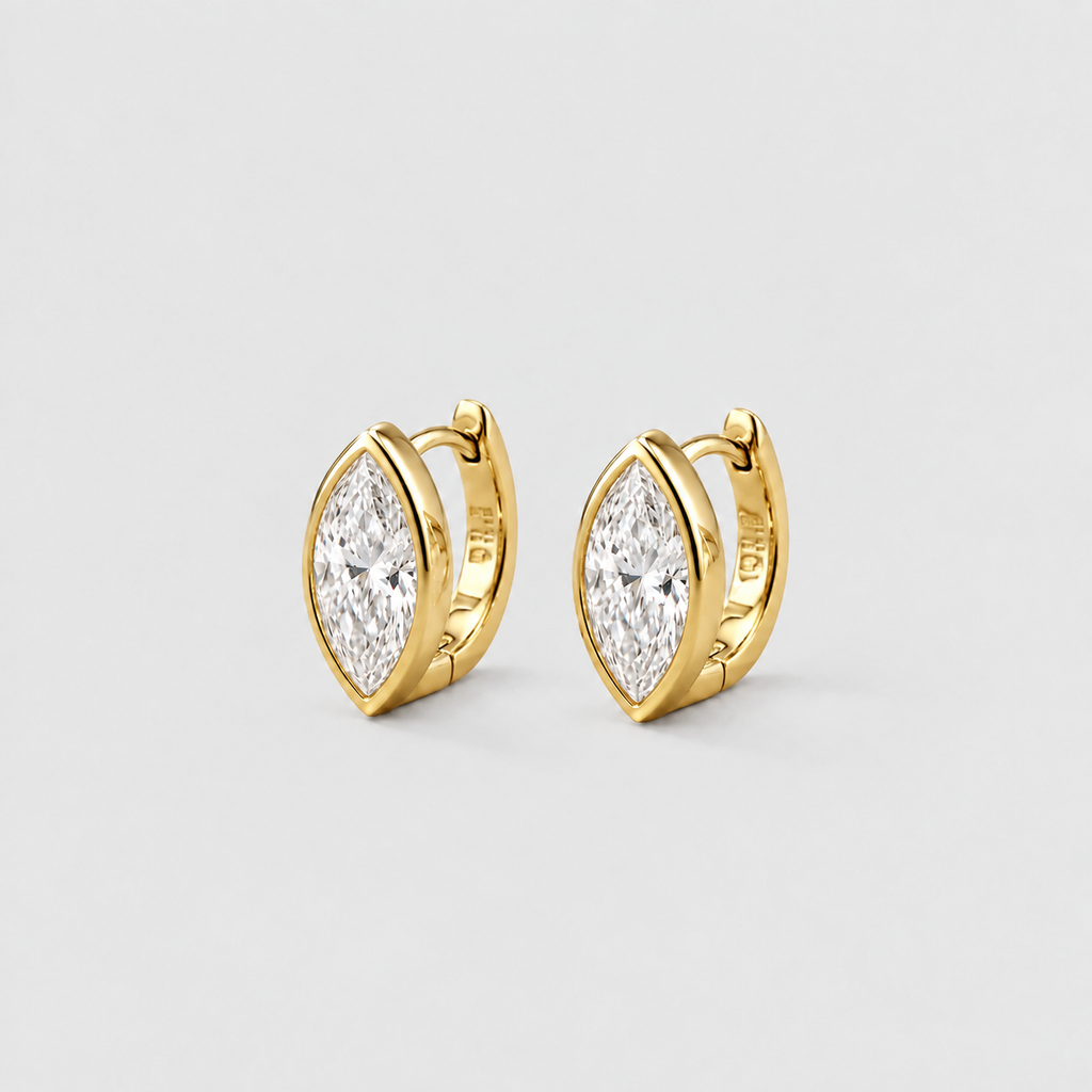 A pair of gold huggie hoop earrings with marquise-cut clear gemstones, displayed on a light gray background.