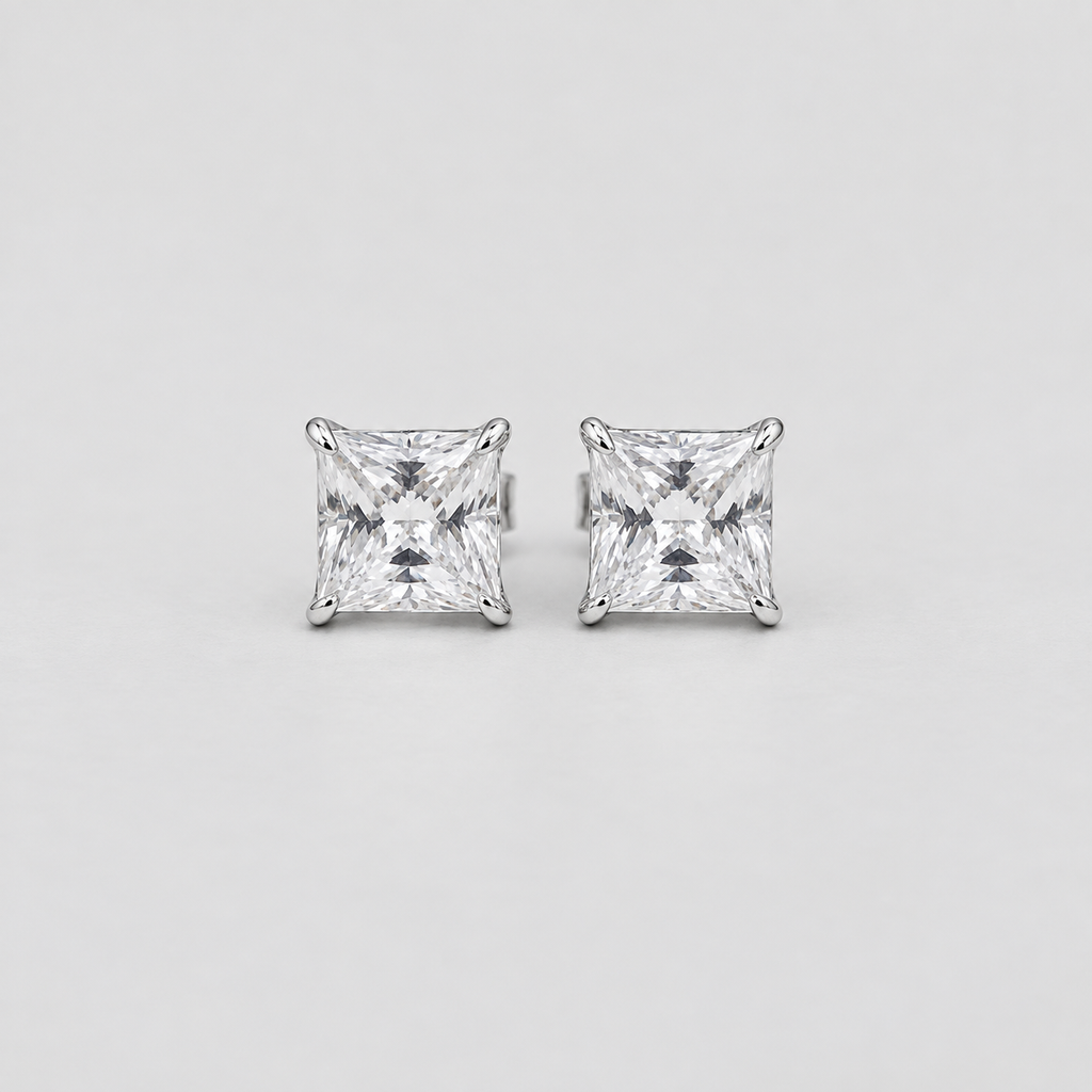 A pair of princess-cut diamond stud earrings in a silver-toned setting, displayed on a clean, light gray background.