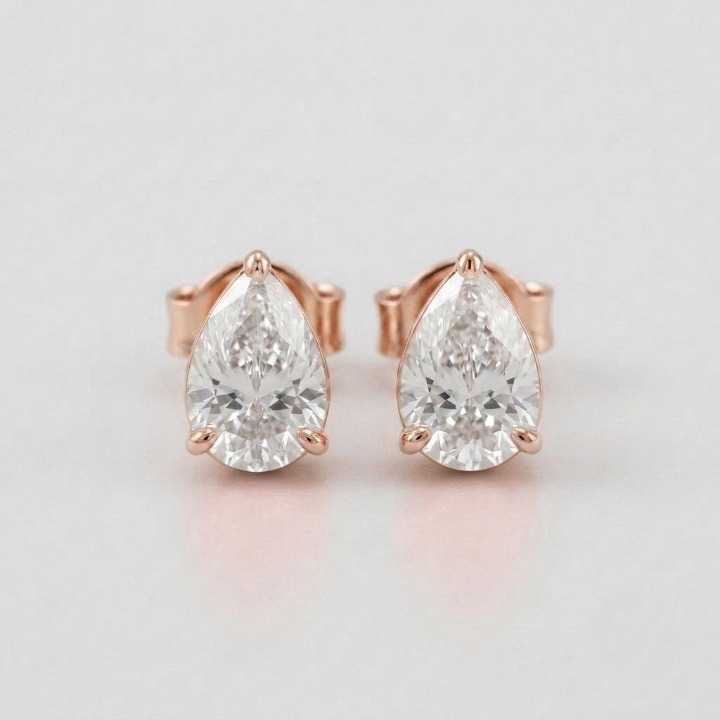 A pair of pear-cut diamond stud earrings in rose gold settings, displayed on a clean light gray background.