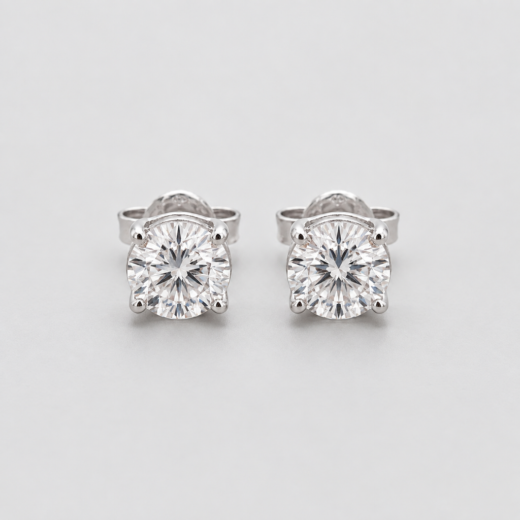 A pair of round-cut solitaire stud earrings in a silver-toned setting, displayed on a clean light gray background.