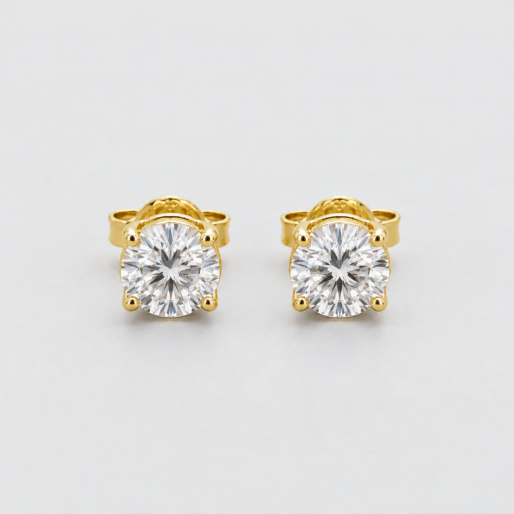 A pair of yellow gold stud earrings with large round brilliant-cut clear gemstones in a four-prong setting, shown on a light gray background.