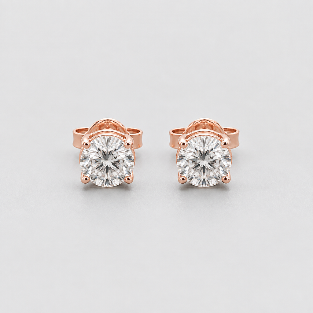 A pair of rose gold stud earrings with round-cut clear gemstones in a four-prong setting, displayed on a light gray background.