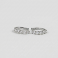 A pair of silver huggie hoop earrings set with a row of clear round-cut gemstones, photographed on a clean, light gray background.