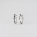 A pair of silver hoop earrings paved with small clear stones, photographed on a clean light gray background.