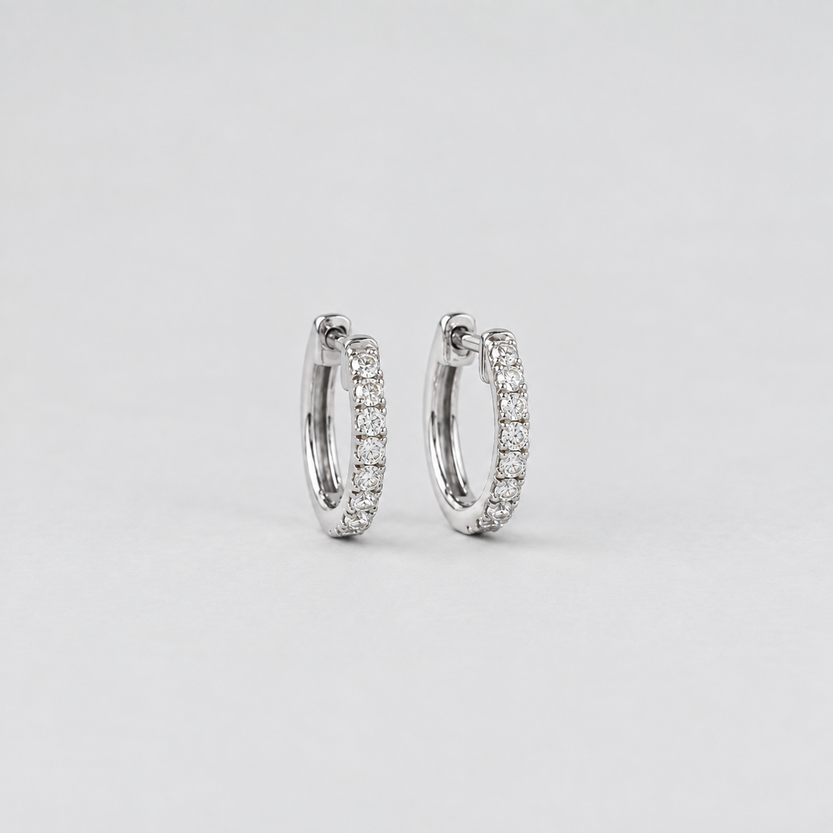 A pair of silver hoop earrings paved with small clear stones, photographed on a clean light gray background.