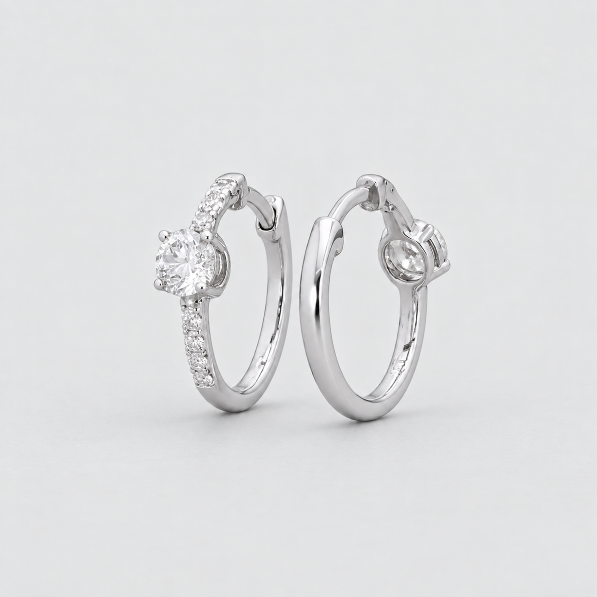 A pair of silver hoop earrings with small pavé-set clear stones and a central round-cut stone, photographed on a clean light gray background.