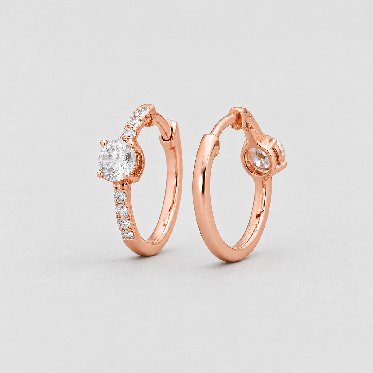 Rose gold hoop earrings with a round-cut center stone and small pavé-set accent stones, shown on a light gray background.