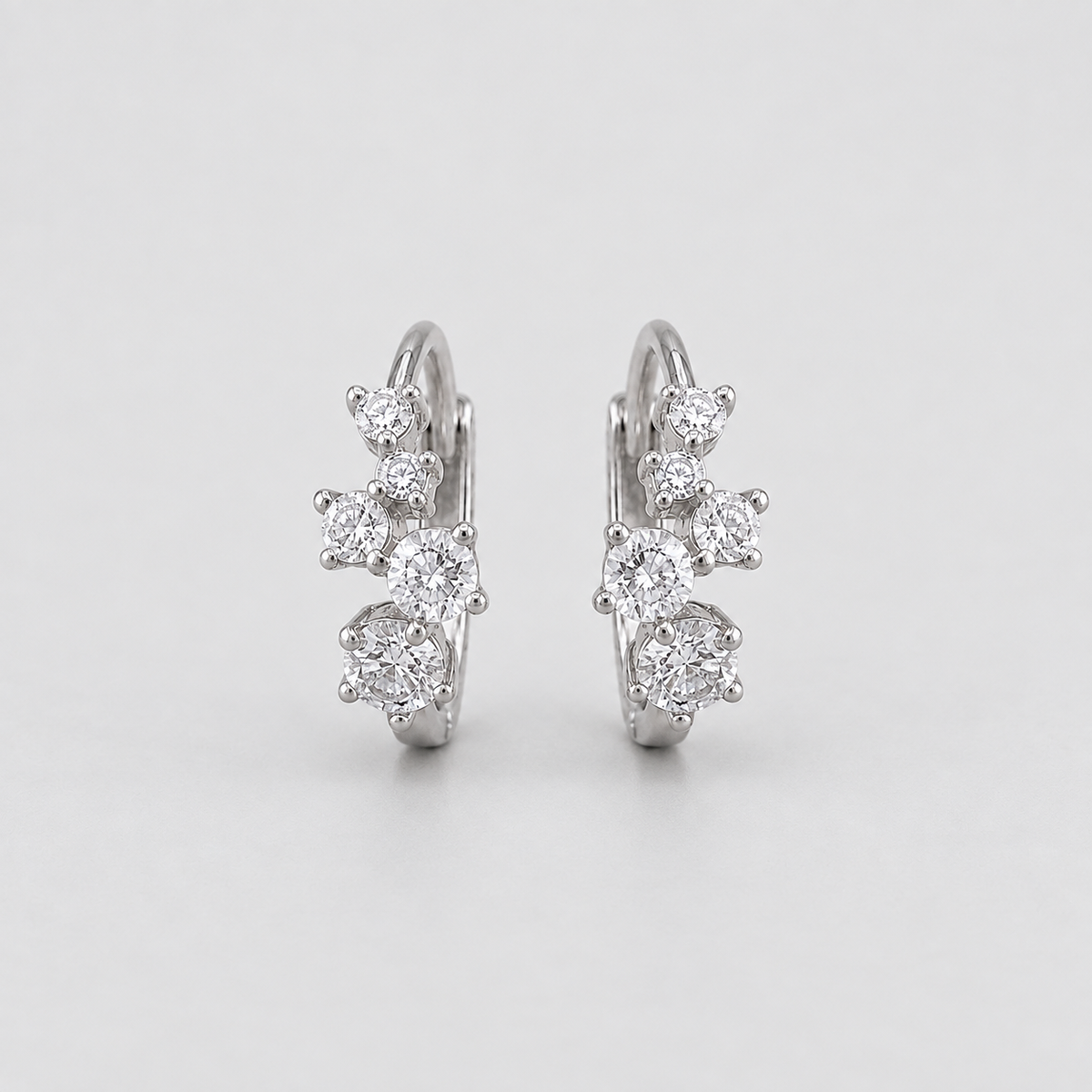 A pair of silver hoop earrings with clusters of clear round-cut and marquise-cut gemstones, photographed on a light gray background.