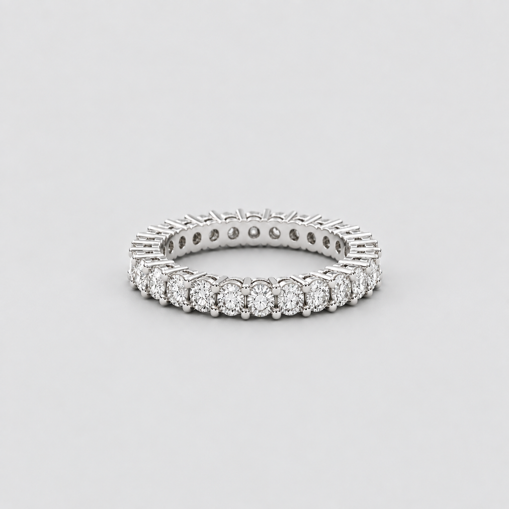 A silver diamond eternity ring with a continuous line of round-cut diamonds set in a polished silver band, photographed on a neutral light gray background.