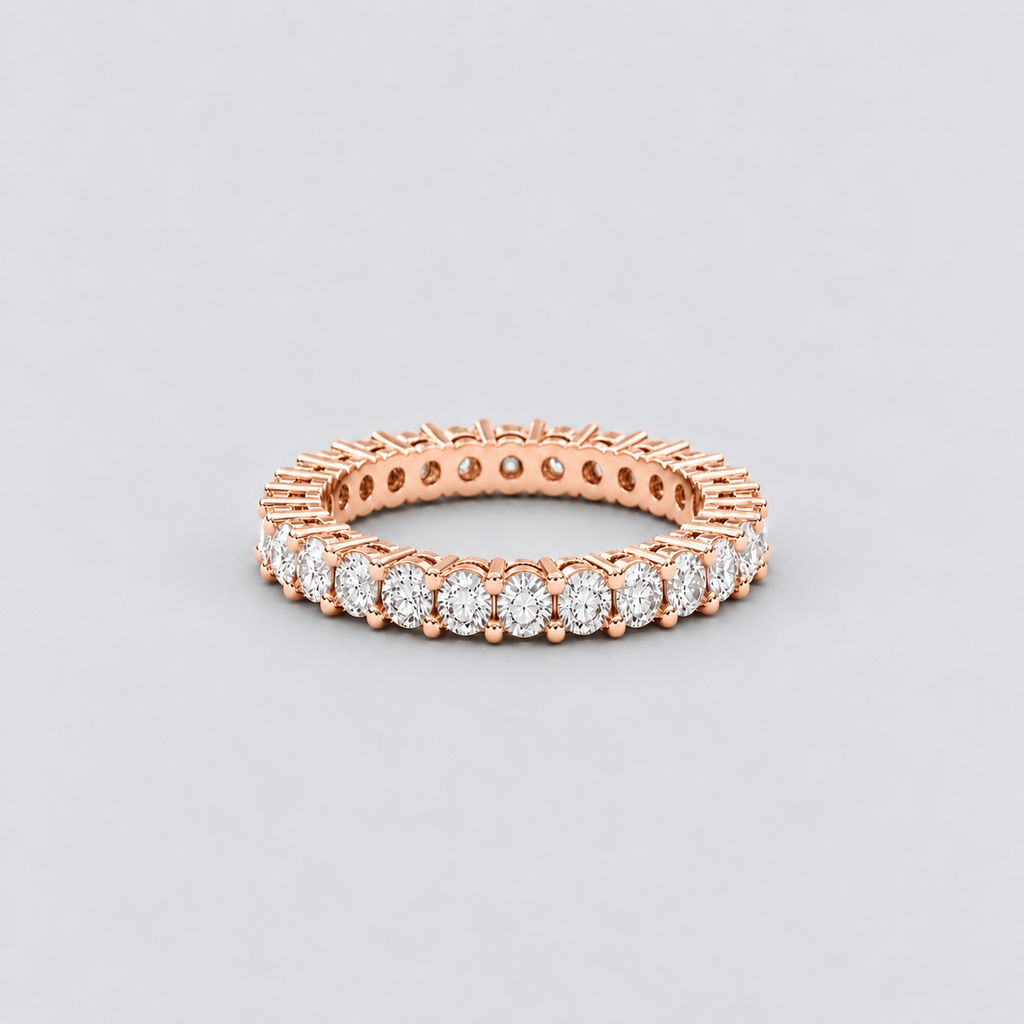 A rose gold eternity ring featuring a continuous row of round-cut clear gemstones, photographed on a neutral light gray background.