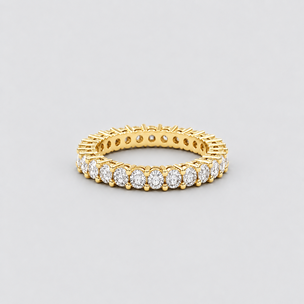 A yellow gold eternity ring featuring a row of round-cut clear gemstones, photographed on a neutral light gray background.