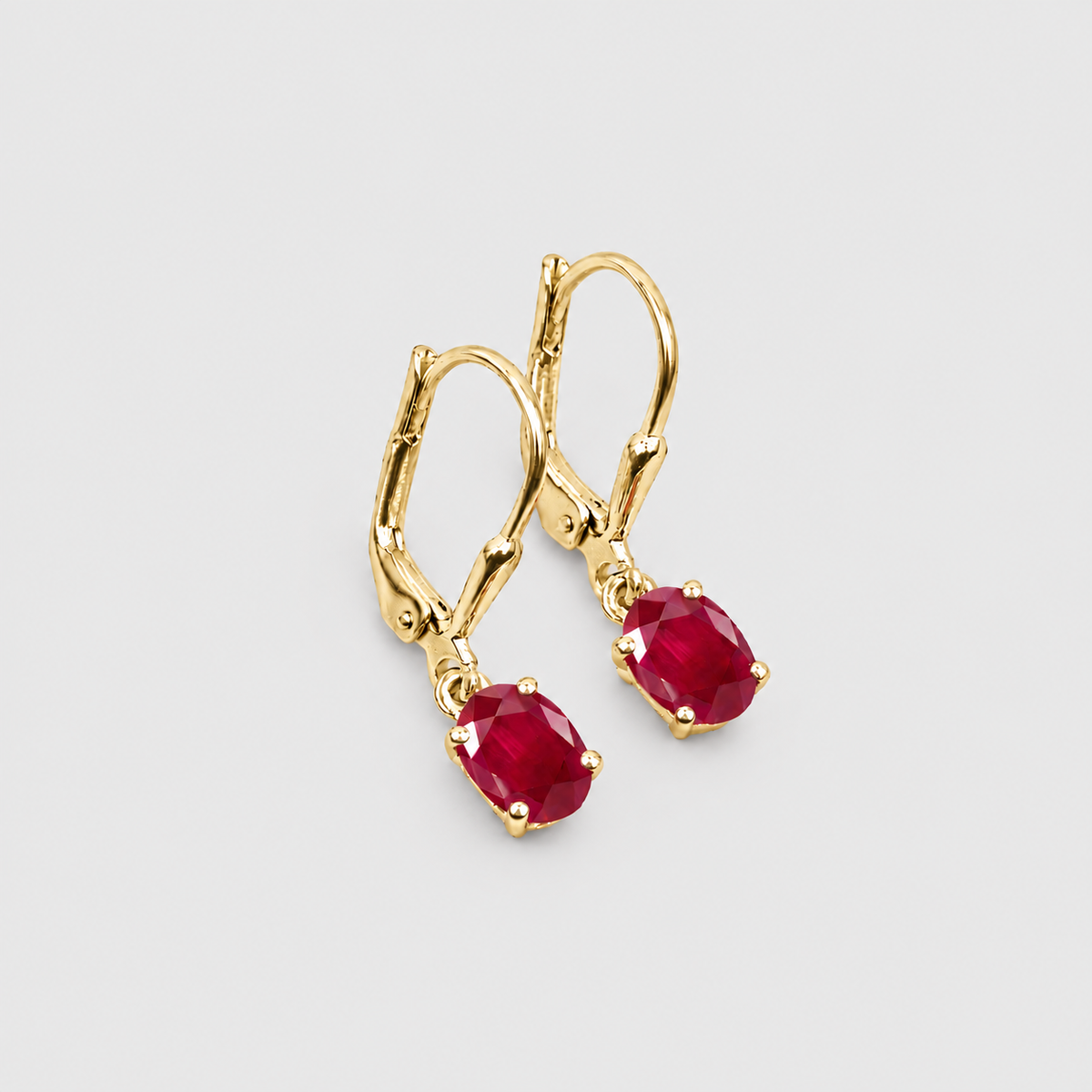 A pair of gold leverback earrings with oval-cut deep red gemstones, shown on a light gray background.