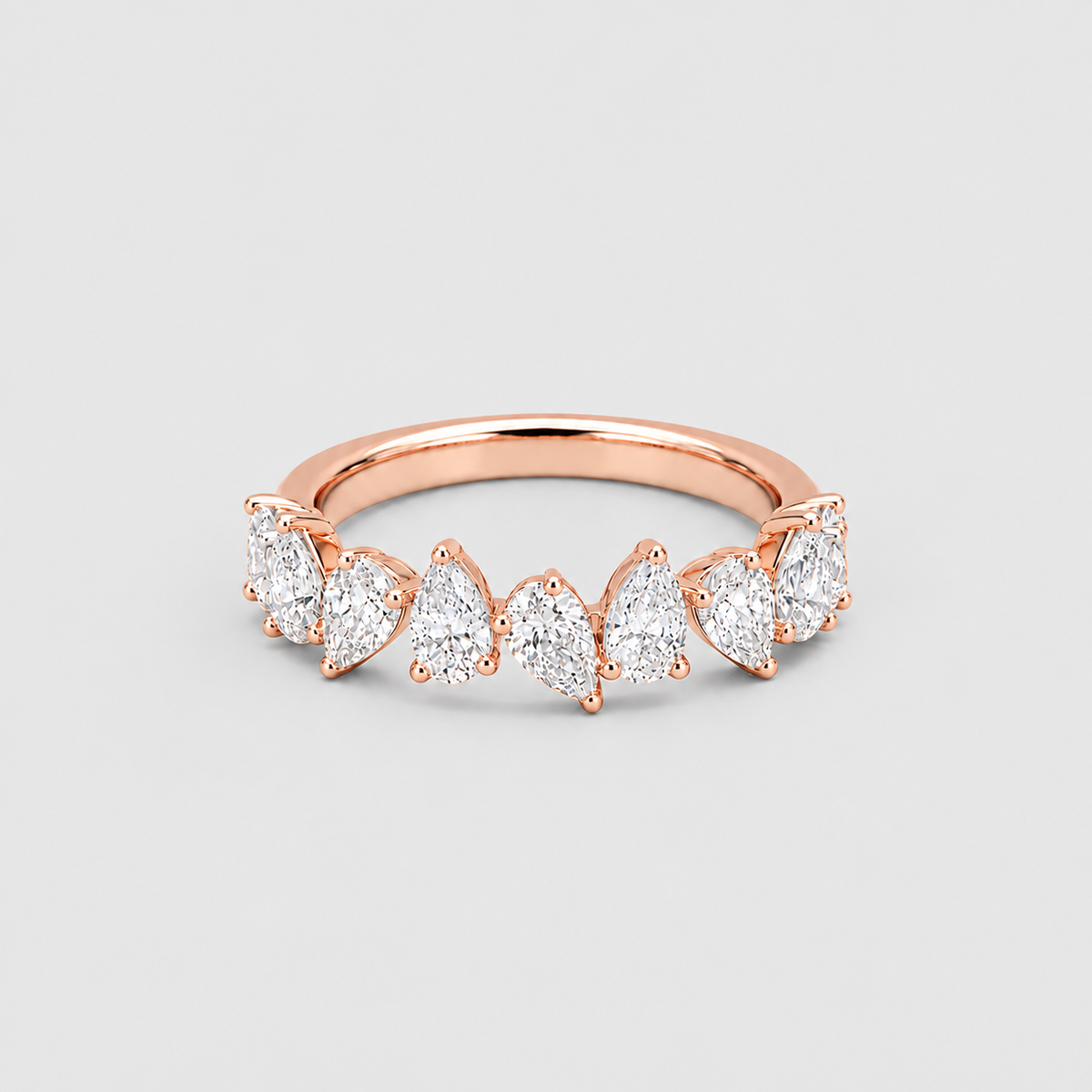 A rose gold ring featuring a row of marquise-cut clear gemstones in a prong setting, shown on a neutral light gray background.