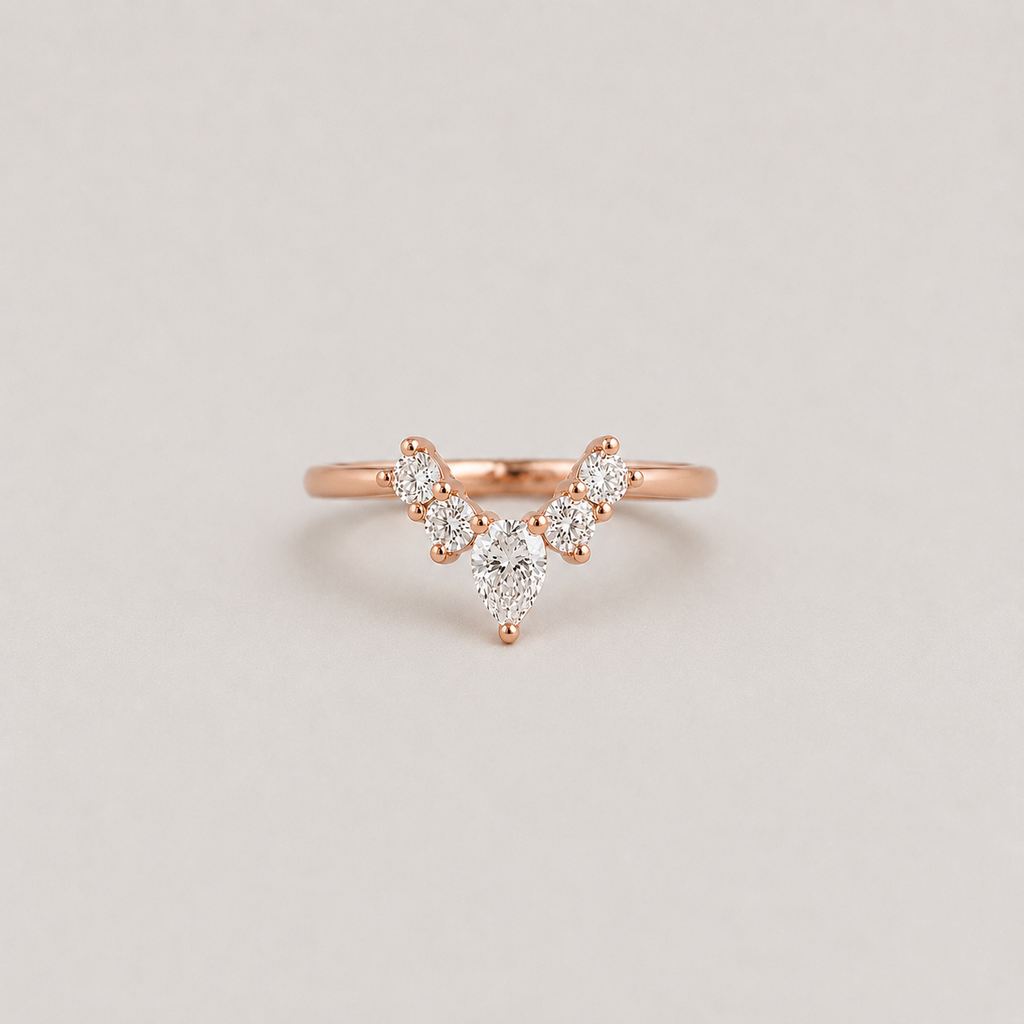 A delicate rose gold ring featuring a V-shaped cluster of small round and pear-cut clear stones, centered on a light gray background.