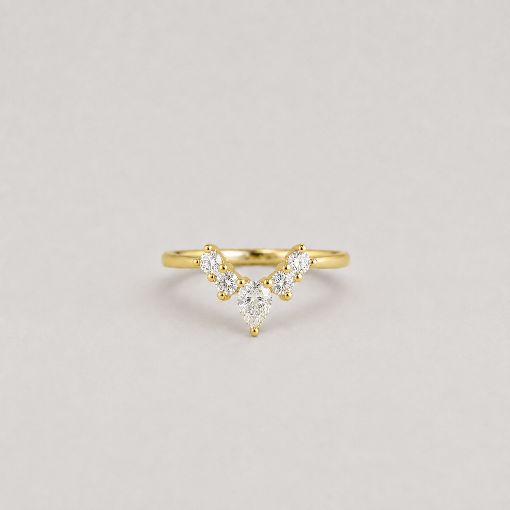 A delicate yellow gold ring featuring a V-shaped cluster of small round and marquise-cut clear gemstones, photographed against a neutral light gray background.