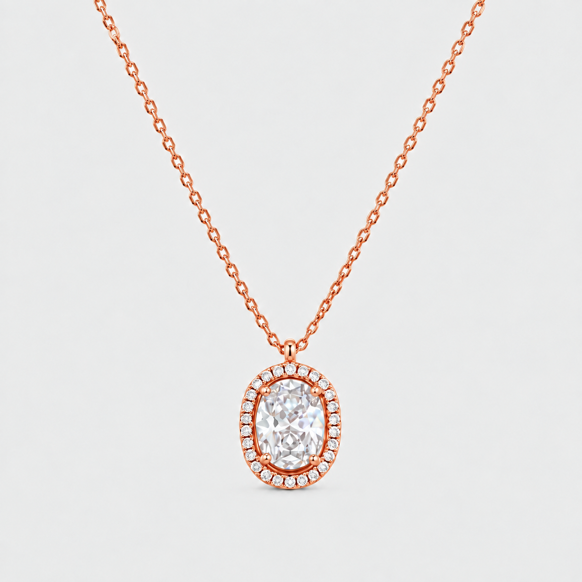 A rose gold necklace with a halo pendant featuring a central oval clear gemstone surrounded by small pavé-set stones, shown on a light gray background.