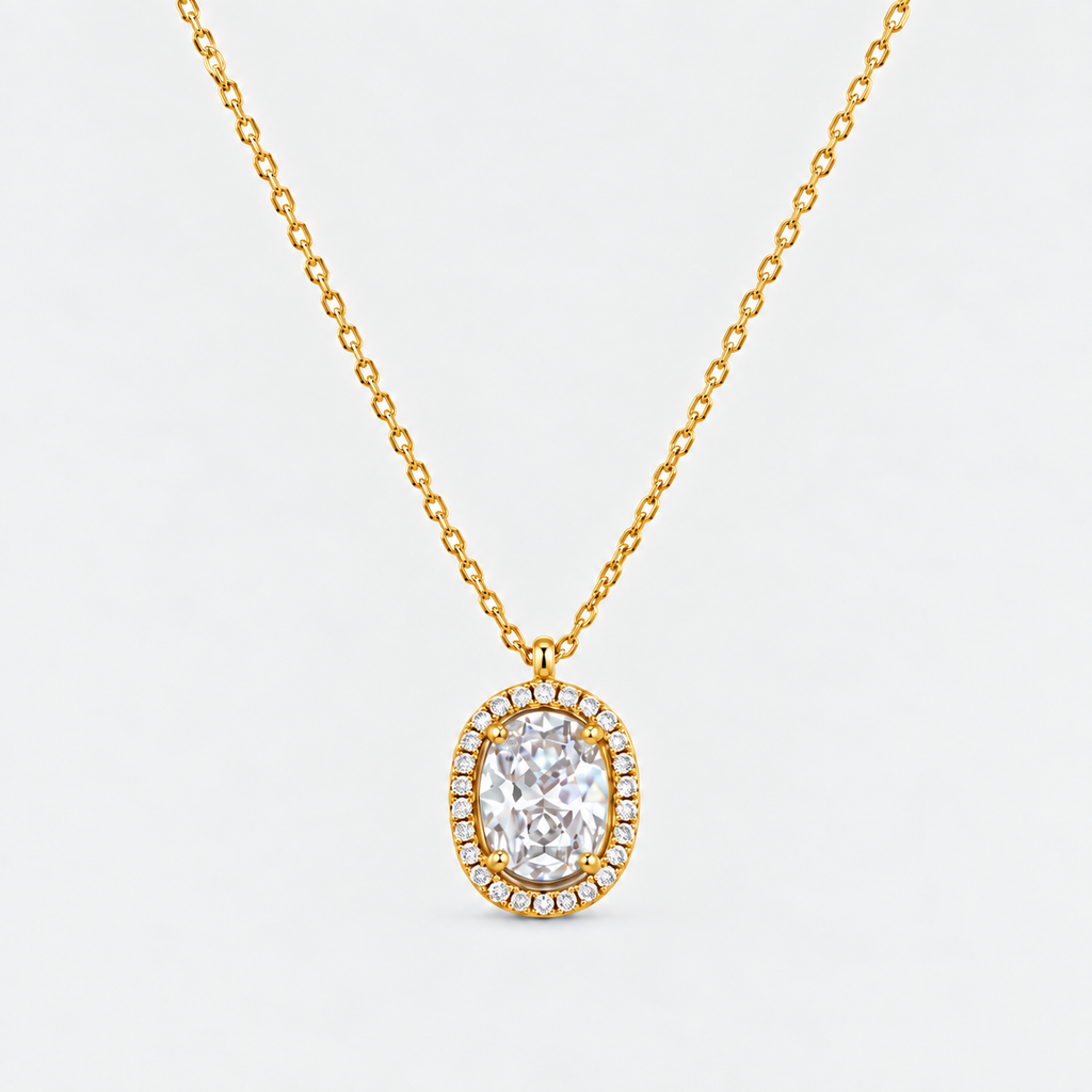 A gold chain necklace with an oval pendant featuring a large clear central stone surrounded by a halo of small clear stones, shown on a light gray background.