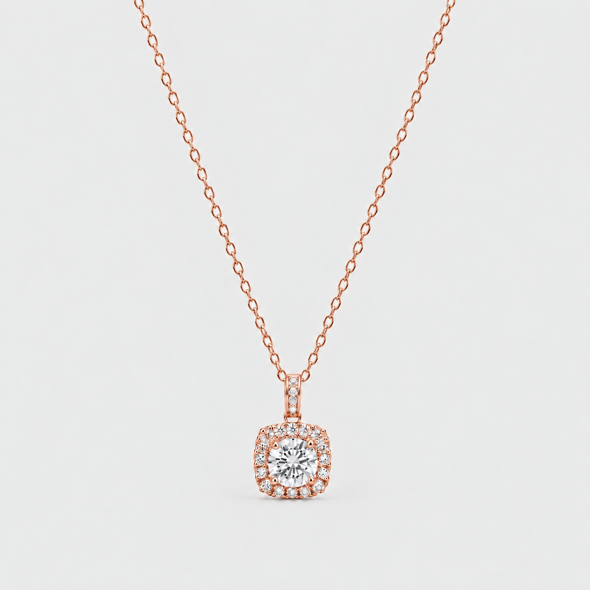 A rose gold necklace with a cushion-cut halo pendant, featuring a central round clear gemstone surrounded by a halo of small pavé-set stones, suspended on a delicate cable chain against a light gray background.
