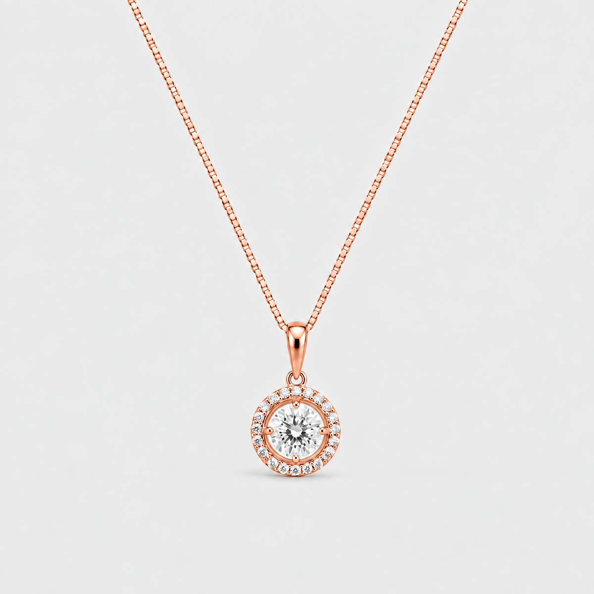 A rose gold necklace with a circular pendant featuring a central clear gemstone surrounded by a halo of small accent stones, set against a light gray background.