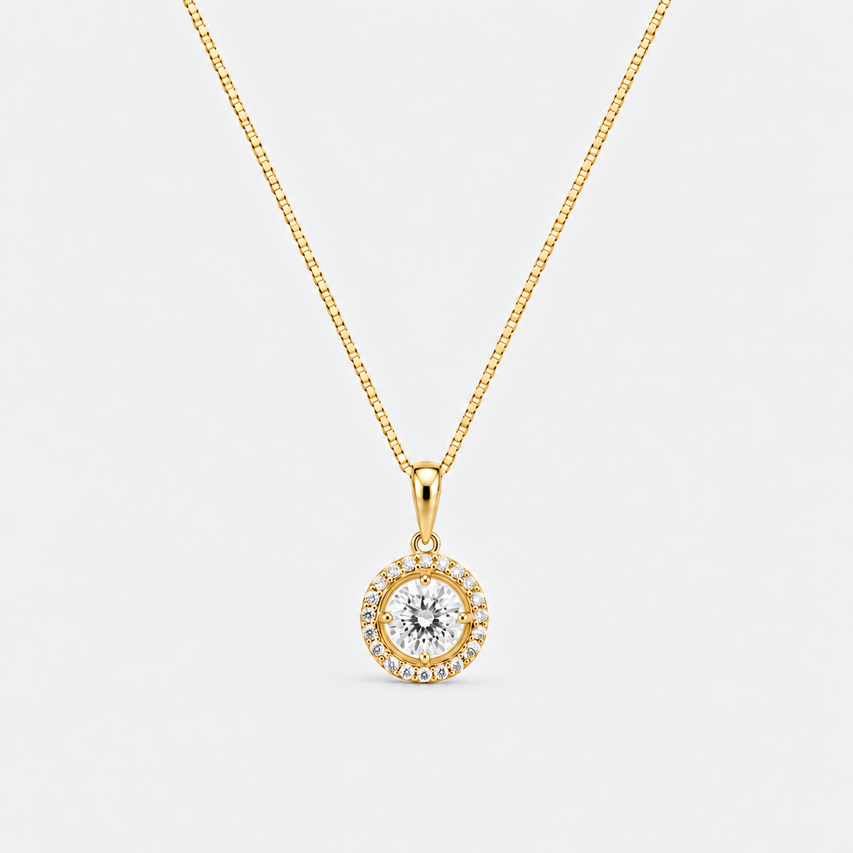 A gold pendant necklace featuring a central round clear gemstone surrounded by a halo of small clear stones, suspended from a gold box chain against a light gray background.