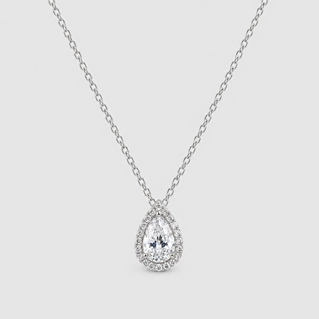 A silver-tone pendant necklace featuring a teardrop-shaped clear gemstone surrounded by a halo of smaller round stones, suspended from a delicate link chain against a light gray background.